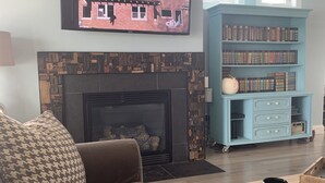 A living room with a fireplace, a sofa, a coffee table, a bookshelf, and a television mounted on the wall. - Industrial chic farmhouse..... (Oshkosh)