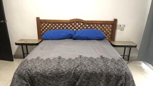Una cama con cabecera de madera, dos mesitas de noche y un edredón estampado.