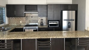 Una cocina moderna con armarios oscuros, encimera de granito, estufa, microondas y refrigerador.