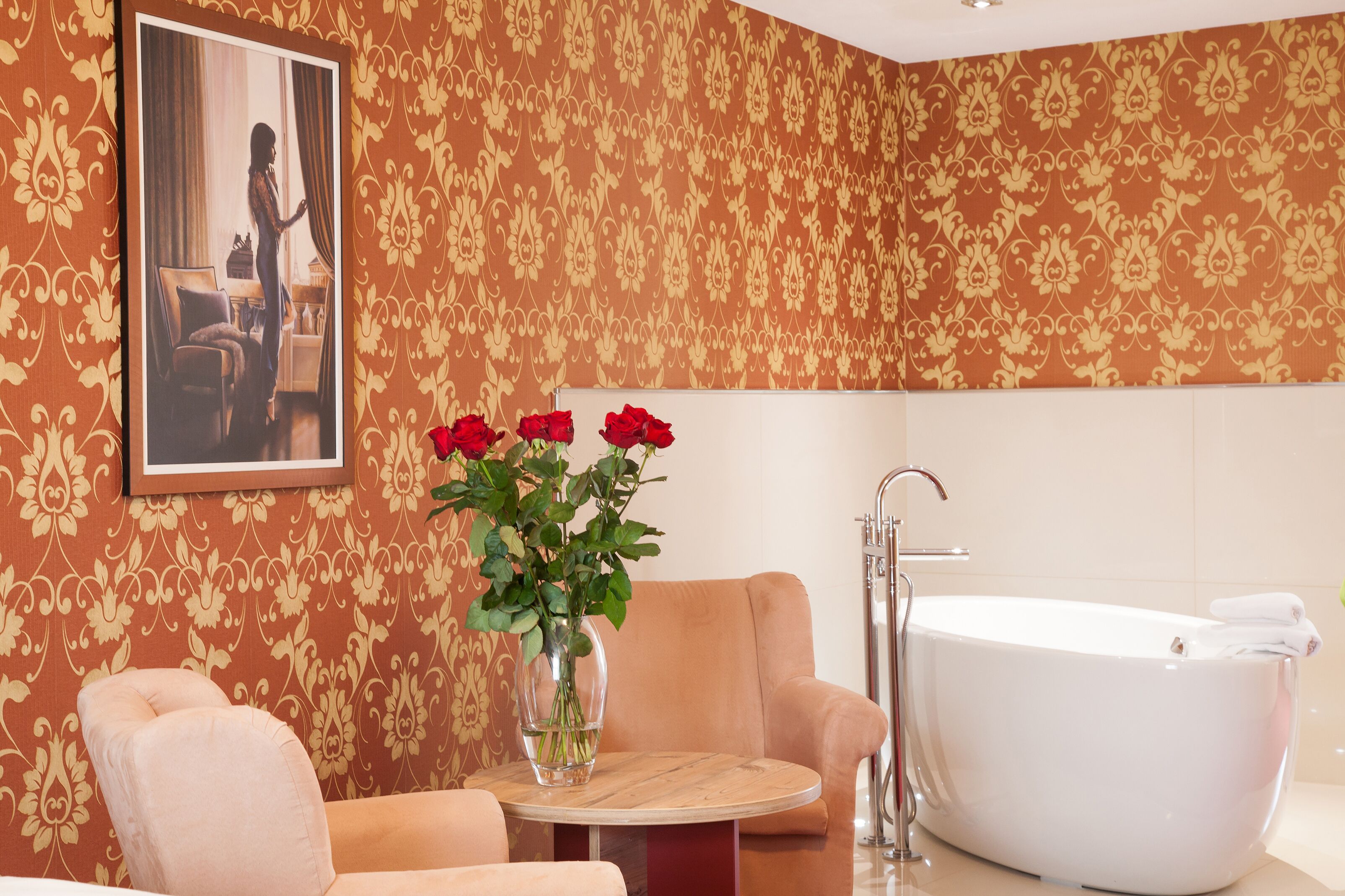 A bathroom with a large bathtub, a round table with a vase of red roses, and a sofa.
