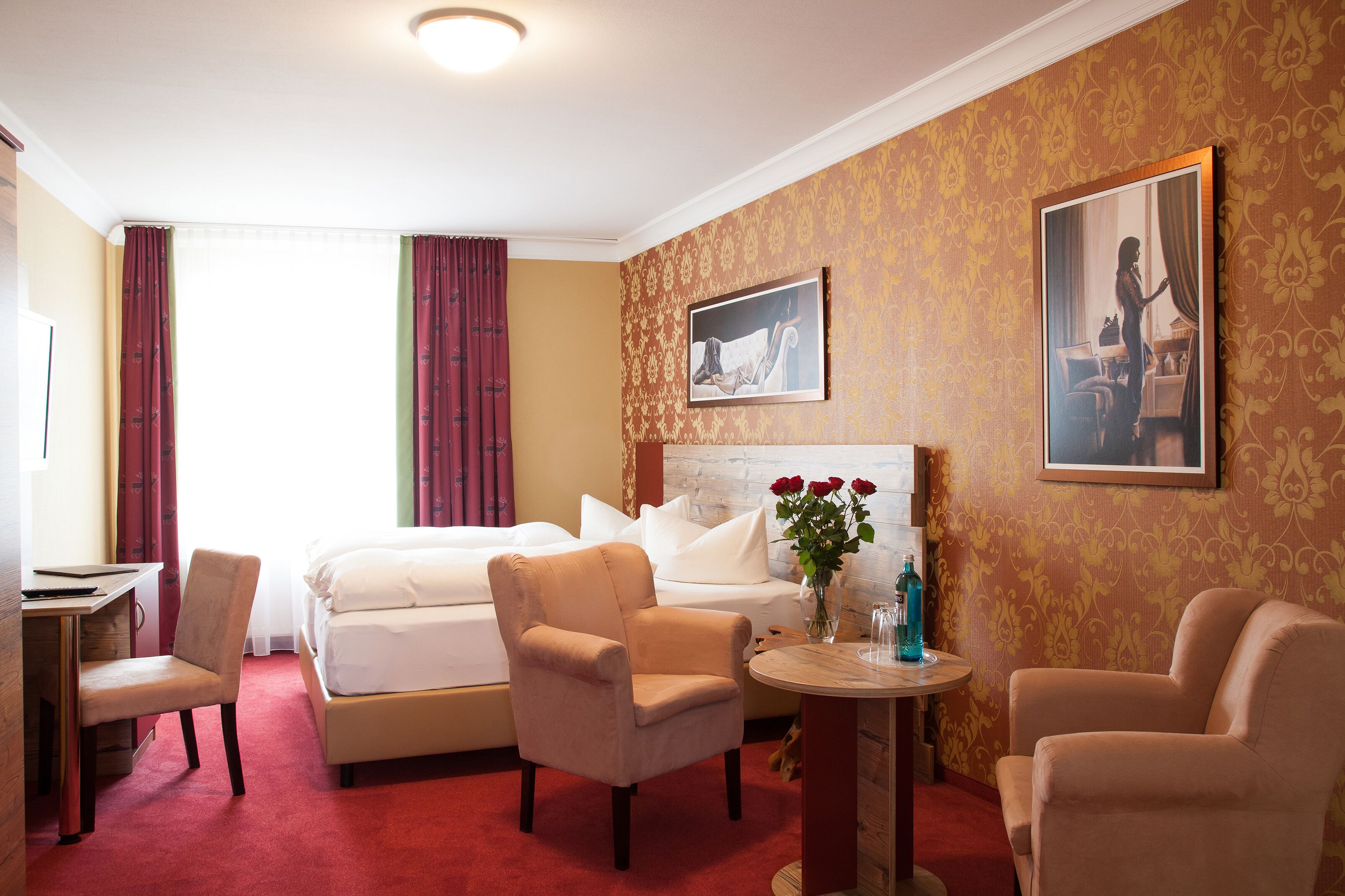 A hotel room with a bed, two armchairs, a small table, and a painting on the wall.