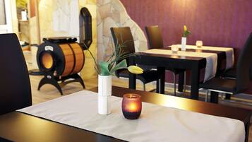 Interior de restaurante con mesas, sillas, una vela y una planta decorativa sobre una mesa.