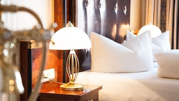 A neatly made bed with white linens and pillows, a bedside lamp, and a wooden nightstand with a power outlet.