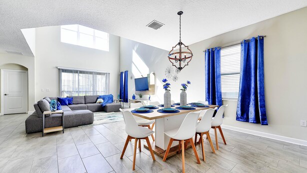 A spacious living area with a dining table, grey sectional sofa, and a large window with blue curtains.