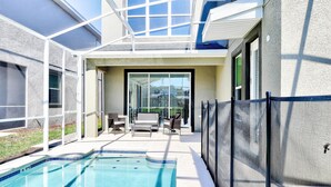 A swimming pool with a glass enclosure, outdoor seating, and a view of the backyard.