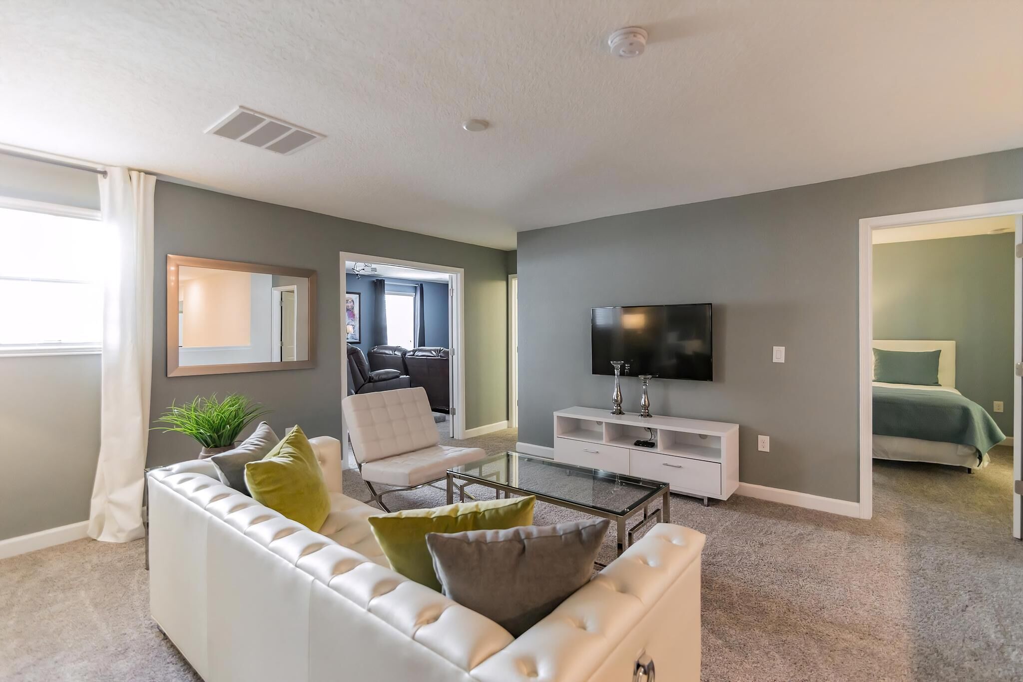 A modern living room with a sofa, coffee table, TV, and a doorway leading to a bedroom.