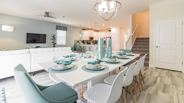 Una cocina moderna con armarios blancos, una isla central y un comedor preparado para seis personas, con decoración en tonos aguamarina y blanco.