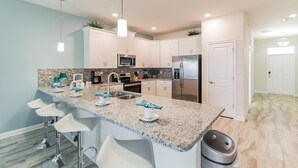 Una cocina moderna con armarios blancos, encimera de granito y electrodomésticos de acero inoxidable, además de taburetes de bar.