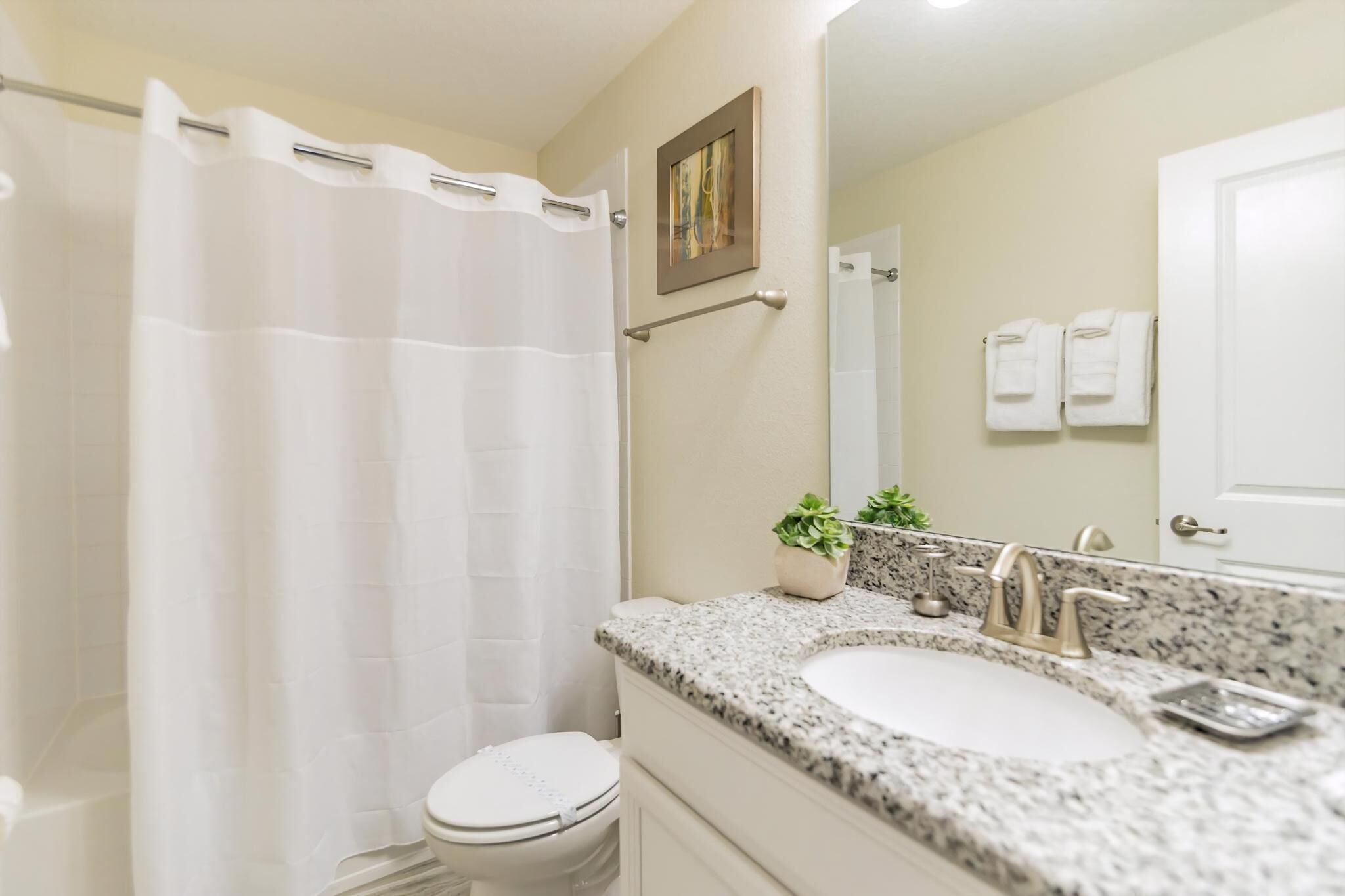 A bathroom with a shower curtain, toilet, sink, and a mirror.