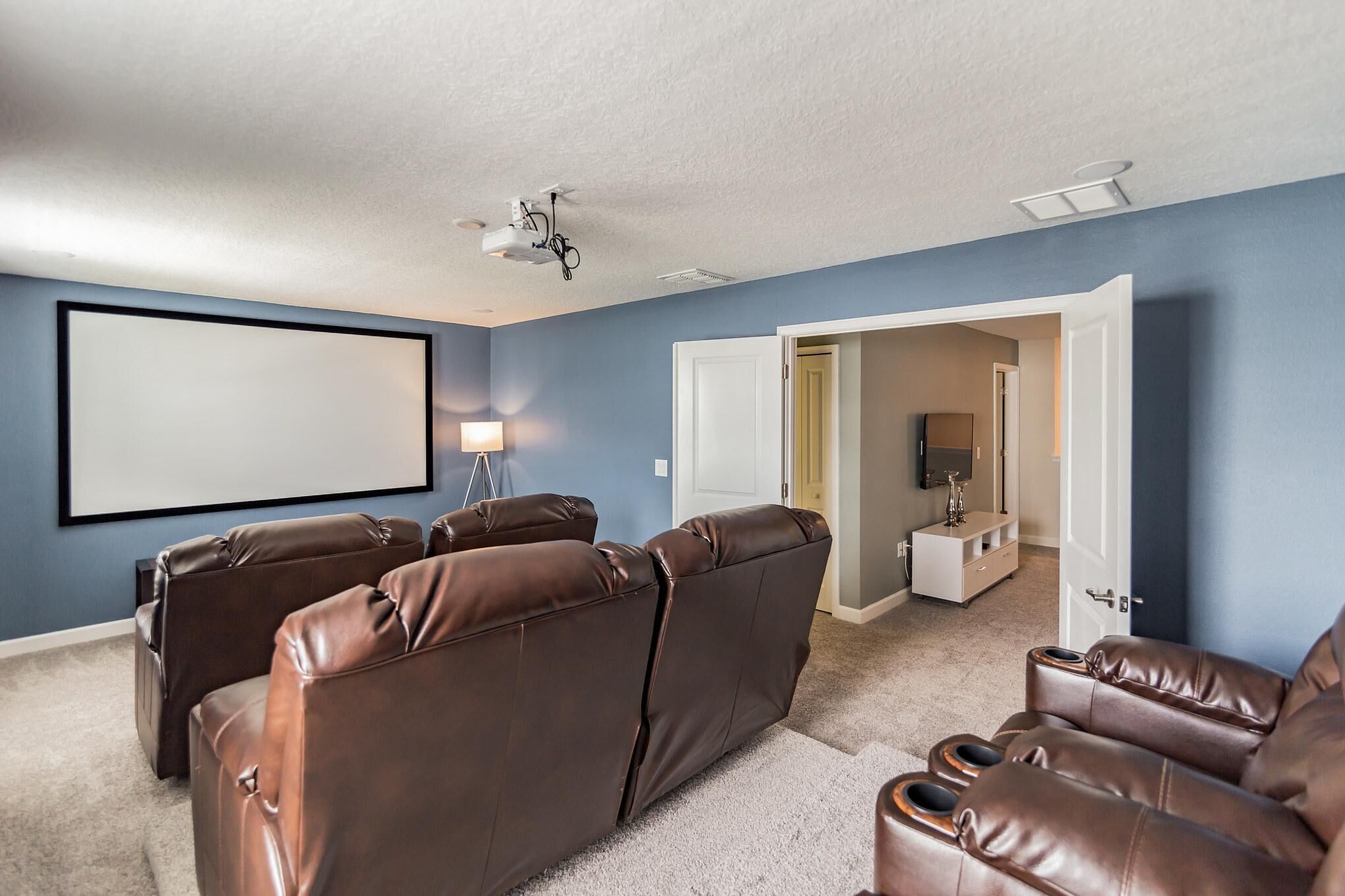 A home theater room with brown leather reclining chairs, a large blank screen, and a ceiling projector.