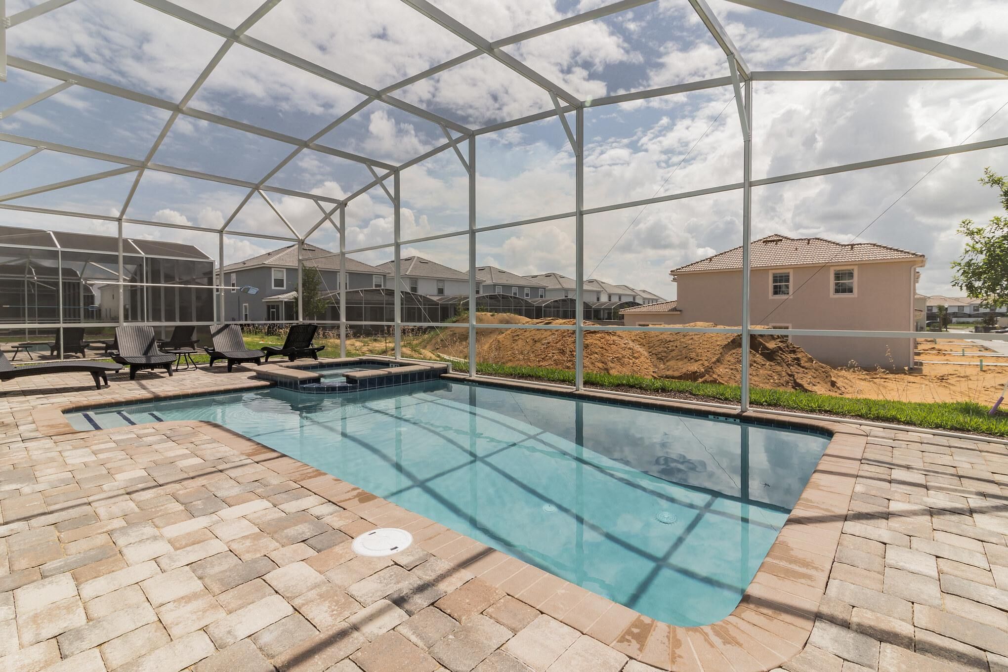 A swimming pool with a glass enclosure, surrounded by a brick patio and outdoor furniture.
