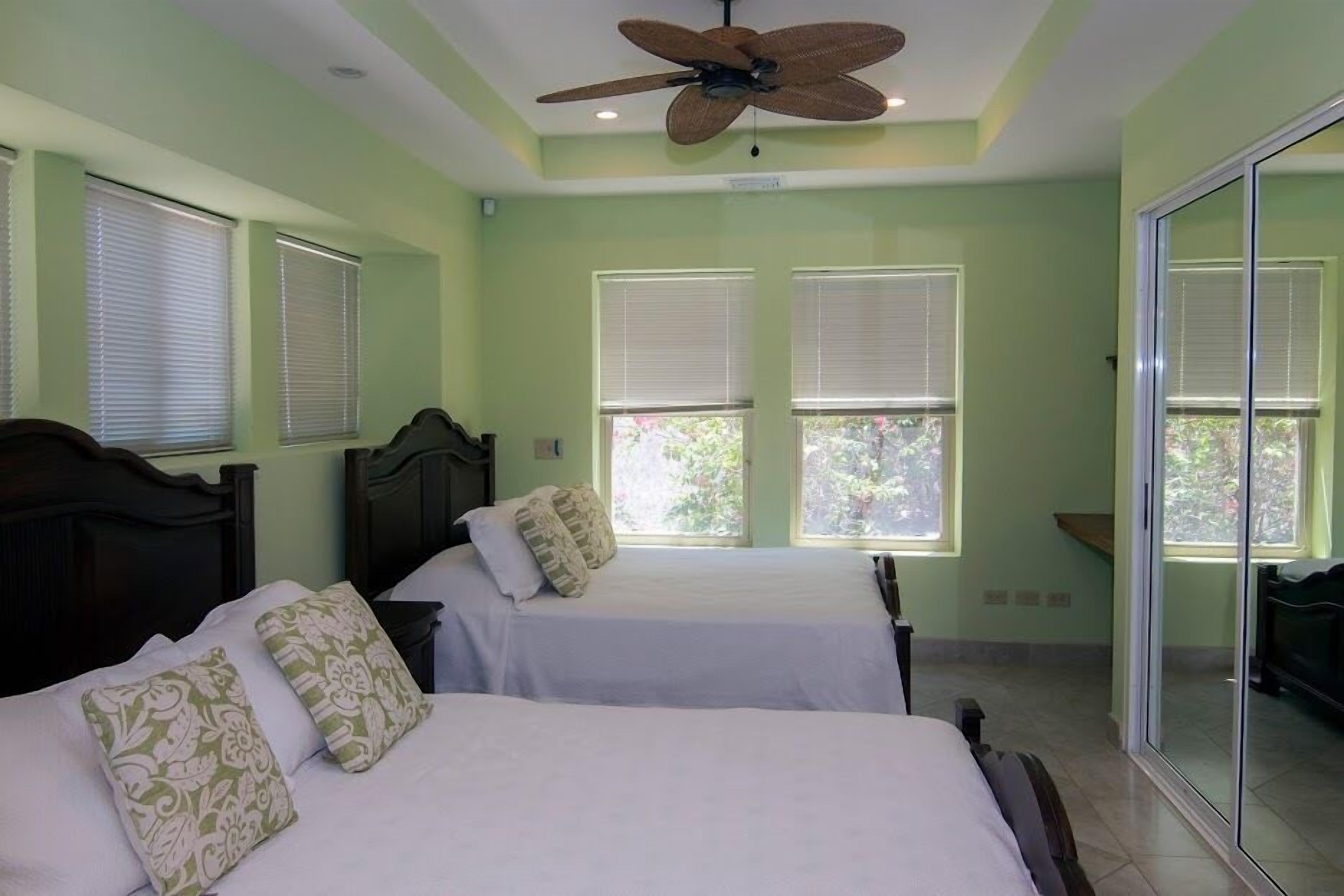 A bedroom with two beds, a ceiling fan, and large windows.