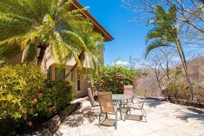 A patio with a table and chairs, surrounded by lush greenery and flowering plants.