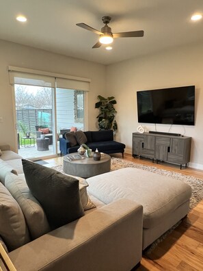 Relax in this stylish living room with a large sectional sofa, flat-screen TV, and sliding glass door leading to an outdoor area.