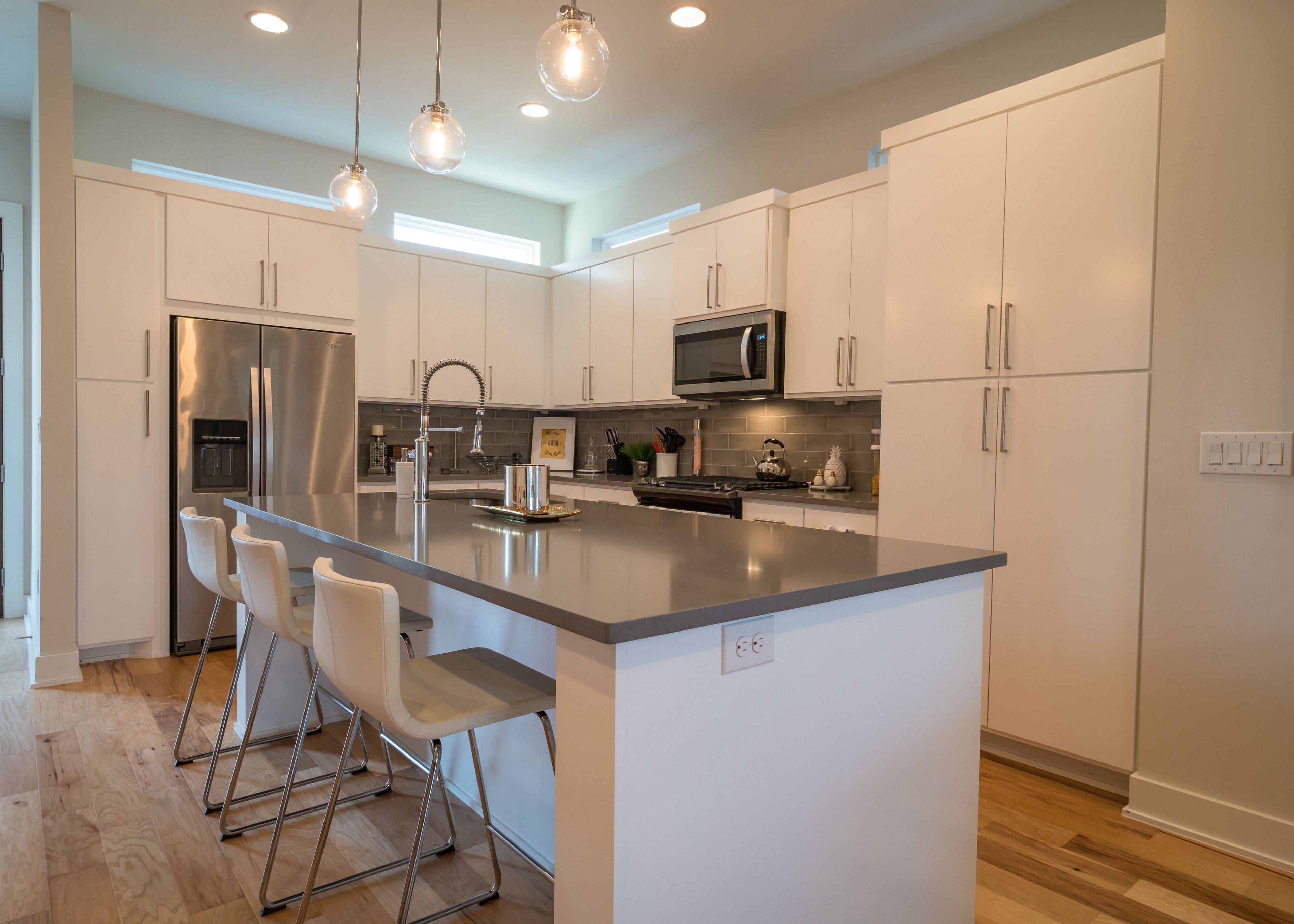 A modern kitchen with white cabinetry, stainless steel appliances, and a central island with bar stools.
