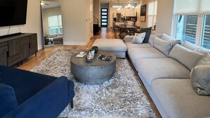 Ein geräumiges Wohnzimmer mit einem großen Sofa, einem Couchtisch und einem an der Wand befestigten Fernseher.