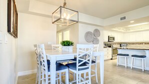 A modern kitchen with white cabinetry, a central island with stools, and a dining area with white chairs and a table.
