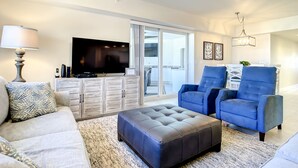 A modern living room with a flat-screen TV, a blue armchair, a grey sofa, and a patterned rug.