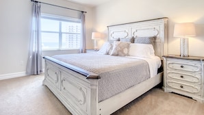 A bedroom with a large bed, two bedside tables with lamps, a ceiling fan, and a window with curtains.