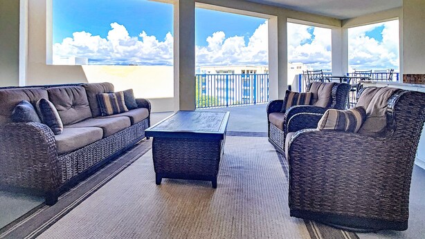 A spacious balcony with a view of the sky and clouds, furnished with a sofa and chairs.