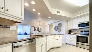A modern kitchen with white cabinetry, stainless steel appliances, and a large island with a dishwasher.