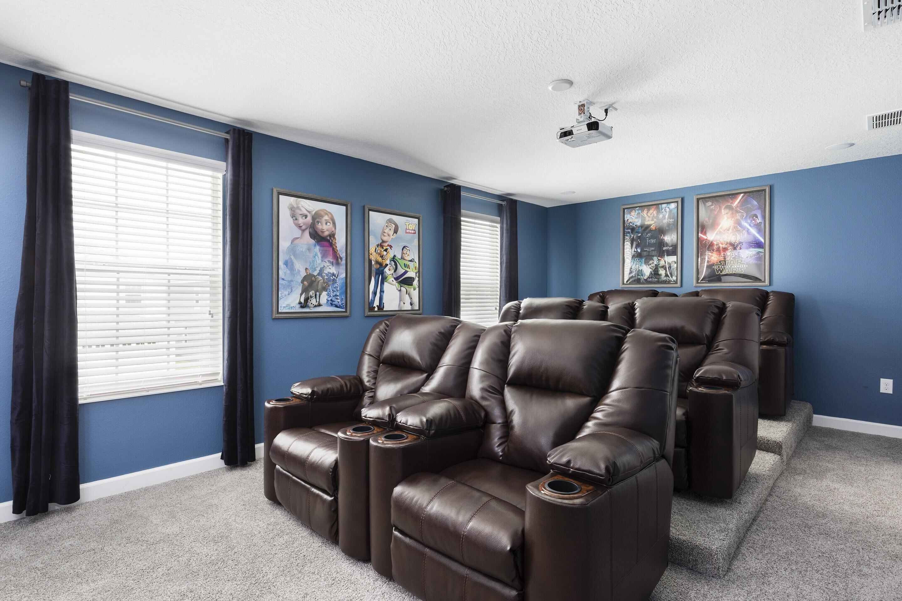 A home theater room with dark brown leather recliners, a ceiling projector, and framed movie posters on the walls.