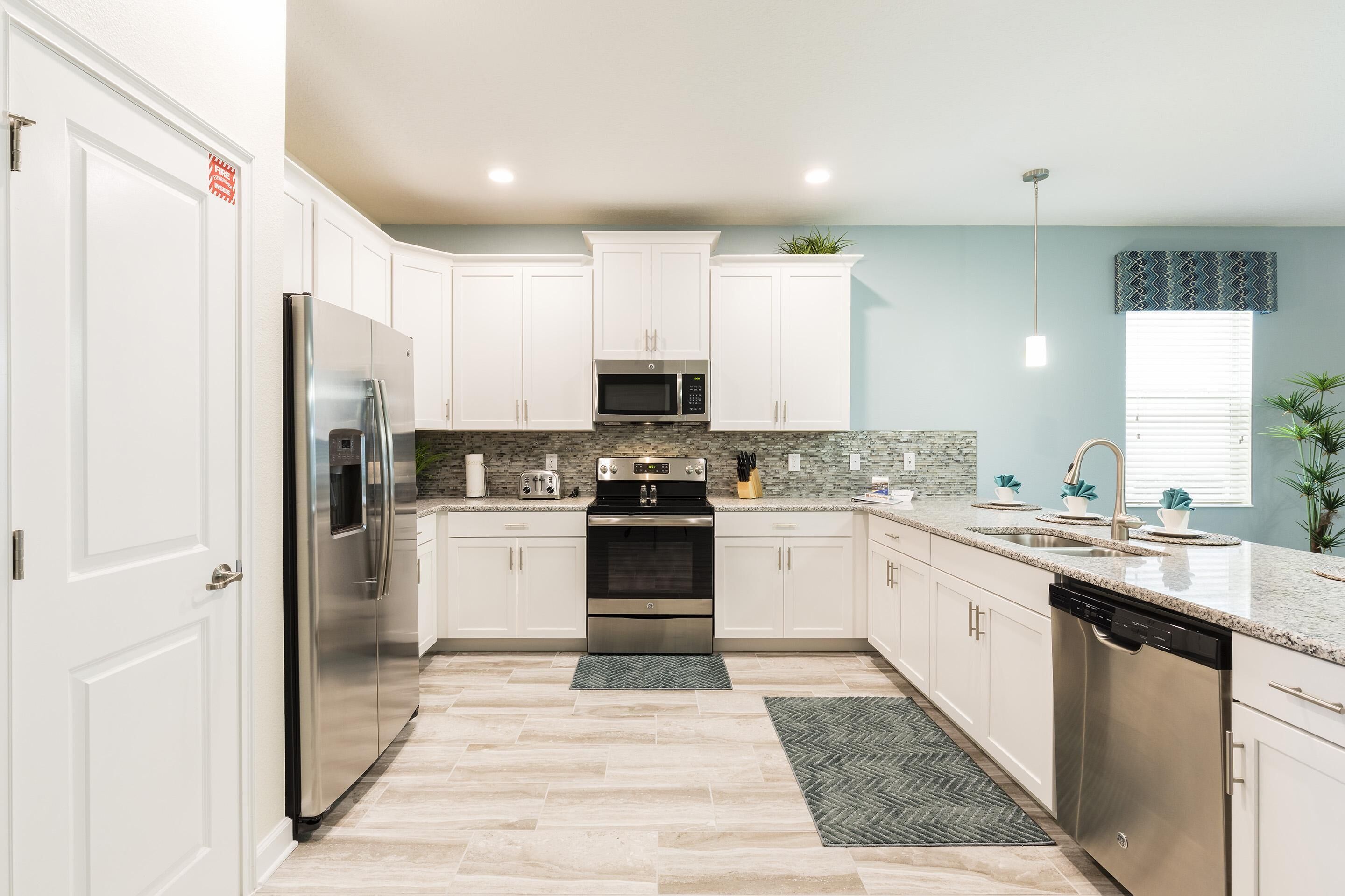 A modern kitchen with white cabinets, stainless steel appliances, a granite countertop, and a herringbone floor pattern.