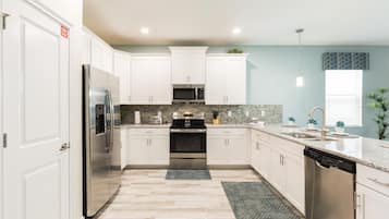 A modern kitchen with white cabinets, stainless steel appliances, a granite countertop, and a herringbone floor pattern.