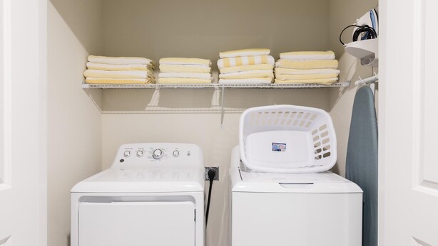 A laundry room with two white washing machines, a drying rack, and a shelf with folded towels. - Tropical Escape by Orlando Short Term (Davenport)