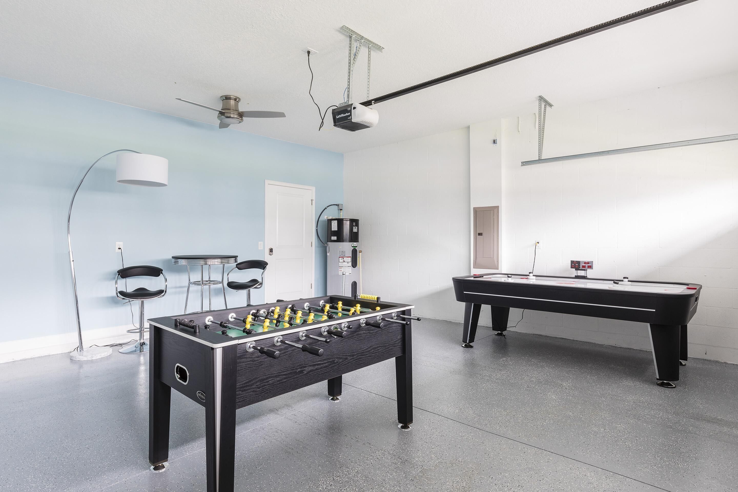 A room with a foosball table, a pool table, and a ceiling fan.