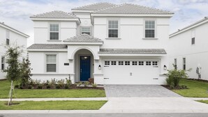 A two-story residential house with a blue front door, a garage, and a well-maintained lawn. - Tropical Escape by Orlando Short Term (Davenport)