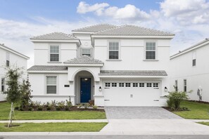 A two-story residential house with a blue front door, a garage, and a well-maintained lawn. - Tropical Escape by Orlando Short Term (Davenport)