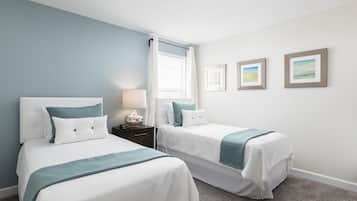 A hotel room with two beds, a nightstand with a lamp, a window with curtains, and three framed pictures on the wall.