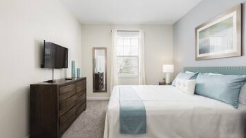 A bedroom with a bed, dresser, TV, and a window with blinds.