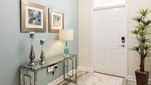 A hallway with a glass console table, two framed artworks, a white door, and a potted plant. - Tropical Escape by Orlando Short Term (Davenport)