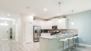 A modern kitchen with white cabinets, stainless steel appliances, and a central island with bar stools. - Tropical Escape by Orlando Short Term (Davenport)