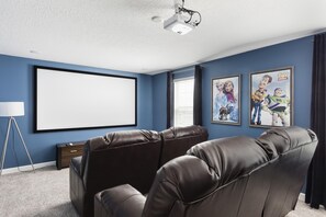 Een bioscoopzaal met een groot scherm, leren loungestoelen, een beamer en ingelijste posters aan de muur.