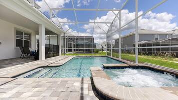 A swimming pool with a hot tub, surrounded by a covered patio area with chairs and a table.