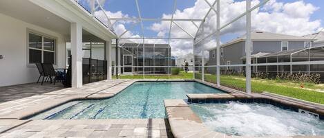 Una piscina con un jacuzzi, rodeada por un patio techado con sillas y una mesa.