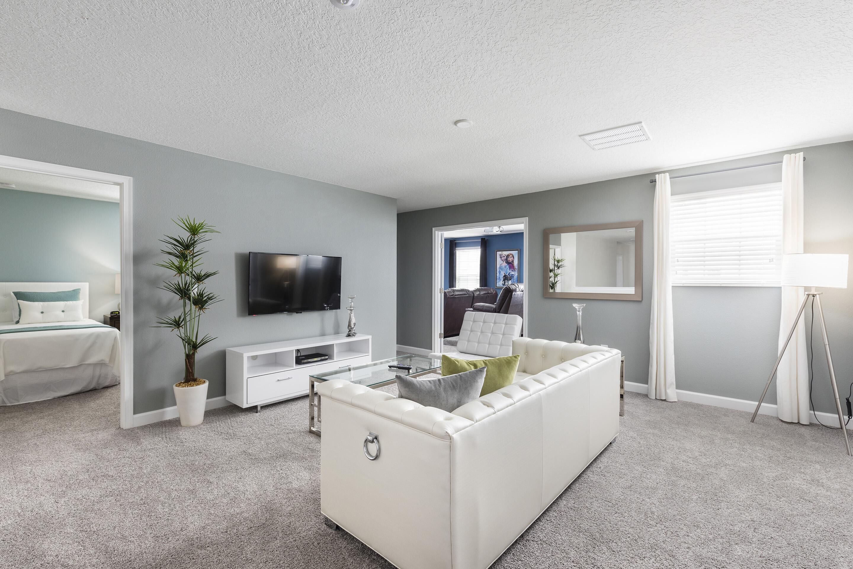 Una sala de estar moderna con un sofá blanco, un televisor de pantalla plana, una mesa de centro y una planta en maceta.