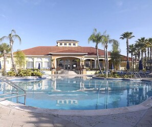 A hotel with a swimming pool, palm trees, and a red-tiled roof.