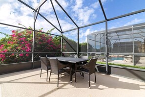A covered outdoor area with a table and chairs, a glass enclosure, and a view of a swimming pool.