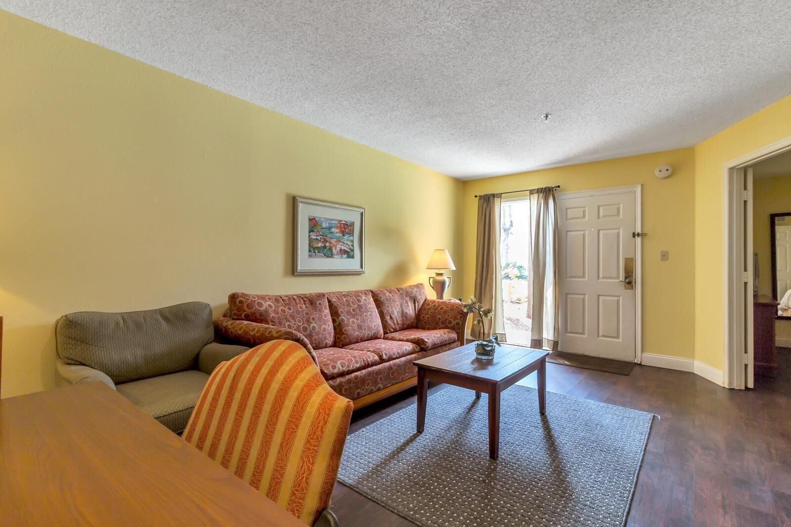 A living room with a sofa, armchair, coffee table, and a painting on the wall.