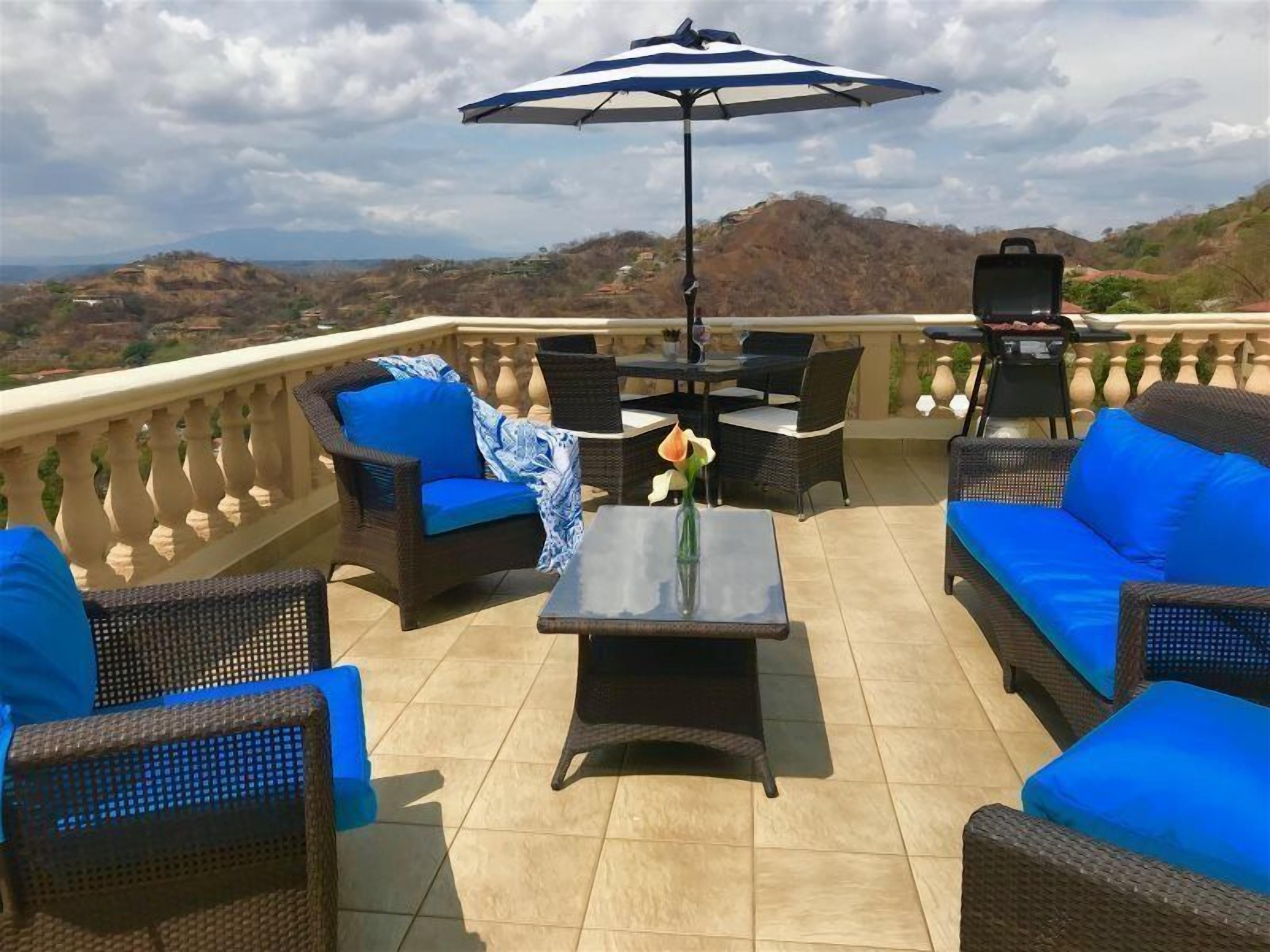 Un patio al aire libre con mobiliario de mimbre, una mesa y una sombrilla.