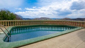 A rectangular swimming pool with a tiled edge and a metal ladder, surrounded by a tiled deck and a balustrade. - Casa Q (Sardinal)