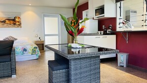 Ein modernes Wohnzimmer mit einem Glastisch, einem Rattansofa, einem Essbereich mit weißen Schränken und einer Küche mit Mikrowelle.