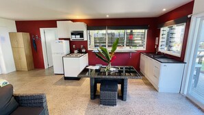 Eine kompakte Küche mit Kühlschrank, Herd und Spüle. Ein Fenster mit Jalousien und ein kleiner Tisch mit einer Vase.
