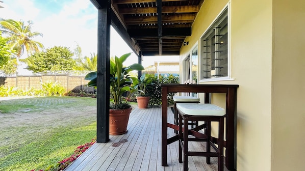 A covered outdoor area with a wooden deck, potted plants, and a table with chairs. - Vaima Studio -steps from the best beach + value for money, air con, free WIFI ! (Vaimaanga Tapere)