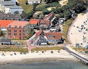 A coastal town with a beach, houses with red roofs, and a bridge connecting the beach to the town.