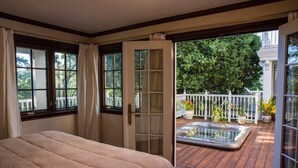 A bedroom with a large bed, a sliding glass door leading to a wooden deck with a hot tub and potted plants. - Mountain View Retreat (Fairfax)